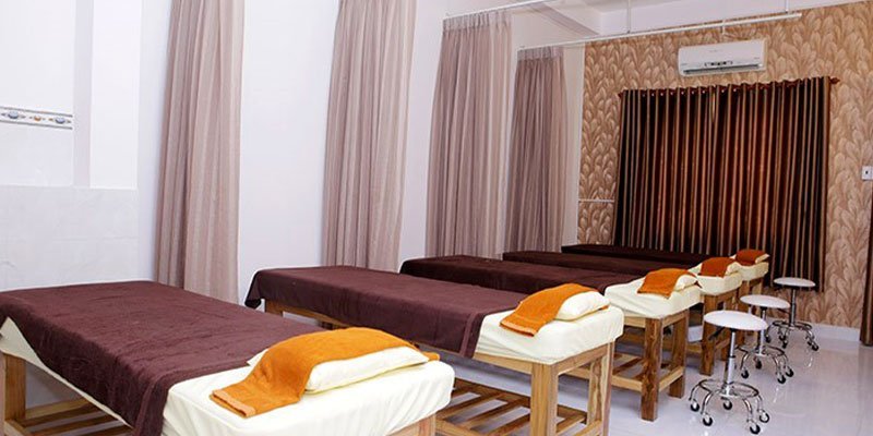 Phòng spa với ba giường massage, khăn màu cam và nâu, không gian ấm cúng với rèm cửa và điều hòa.