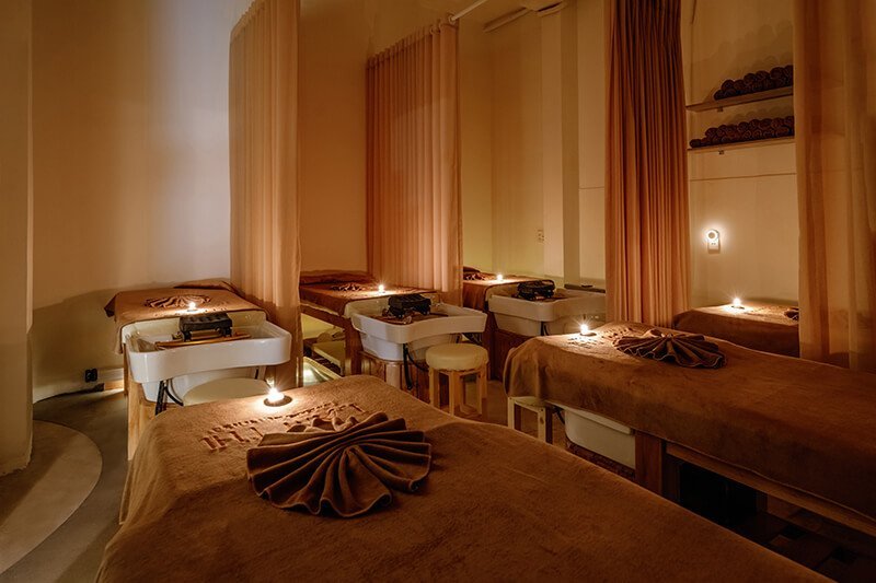 Phòng spa với giường massage, ánh nến dịu nhẹ và rèm vải tạo cảm giác thư giãn.