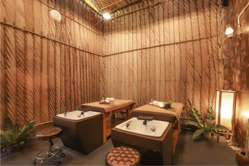 Phòng spa với giường massage, bồn rửa và trang trí cây xanh, ánh sáng ấm áp, tạo cảm giác thư giãn.