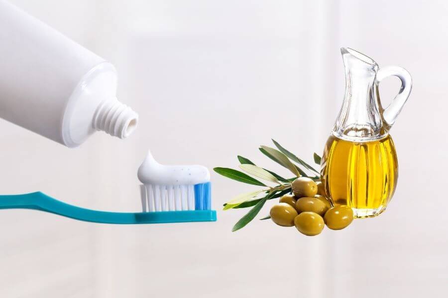 Bàn chải đánh răng với kem, bên cạnh là chai dầu ô liu và vài quả ô liu, biểu tượng của tự nhiên và vệ sinh.